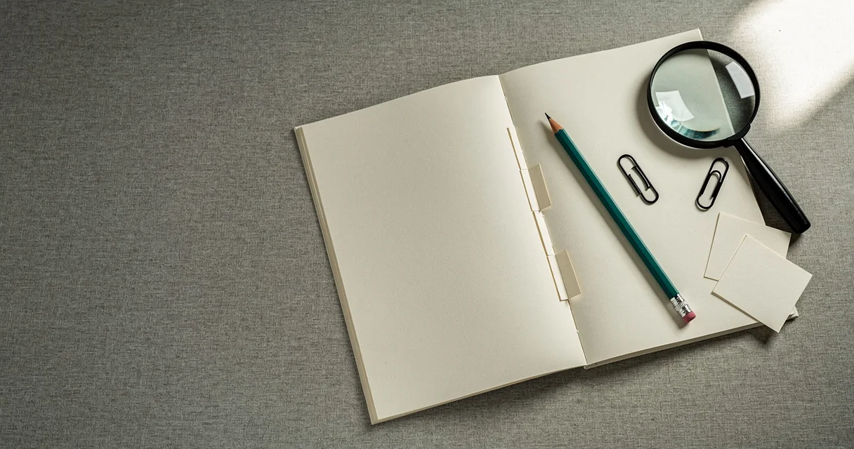 An open paper journal, folded slips and a teal pencil on a light reading table
